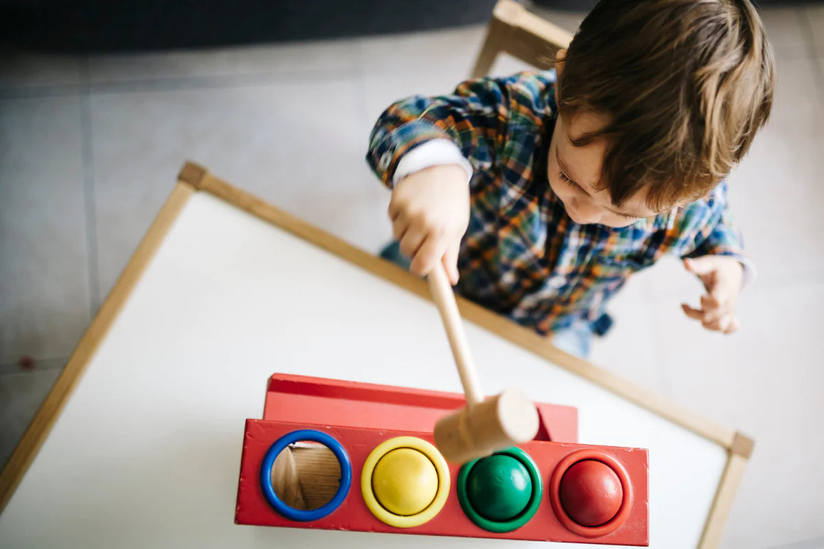 Small child plays with a wooden hammer and ball toy in bright primary colors