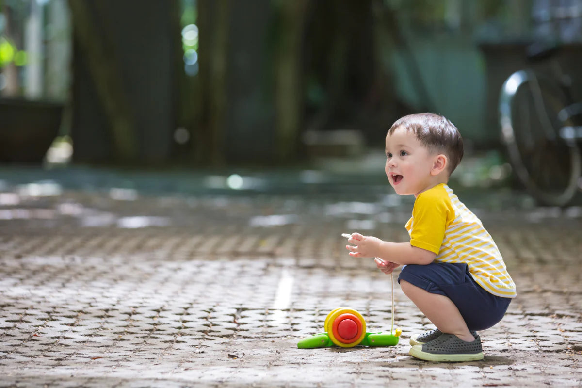 Little boy plays with PlanToys Pull Along Snail in bright red orange yellow and green