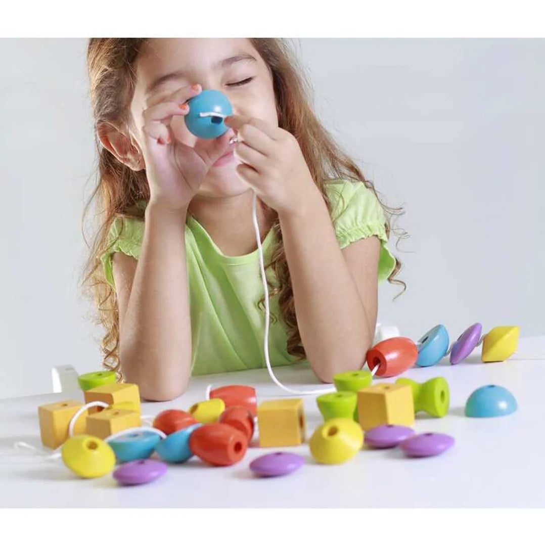 Girl plays with Colorful PlanToys Lacing beads wooden beads with lacing string