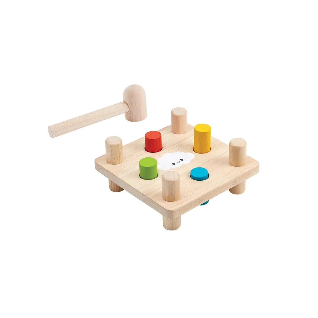 Close up product shot PlanToys Hammer Peg wooden peg and hammer toy with red, blue, yellow, and green pegs on a natural board with mallet.