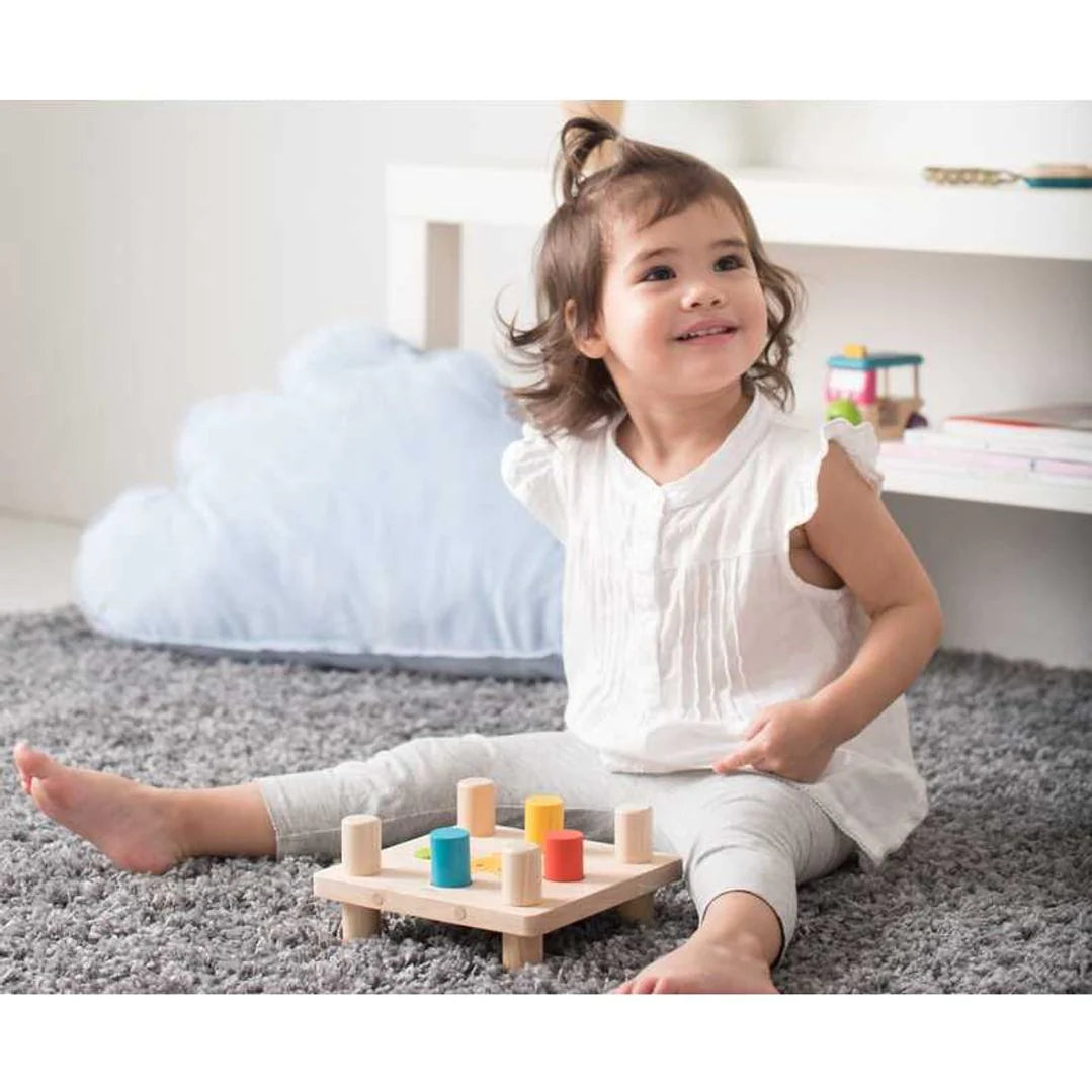 Happy girl plays with PlanToys Hammer Peg wooden peg and hammer toy pounds colorful pegs with wooden mallet