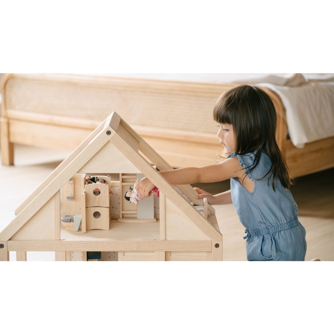 Child plays with My First Dollhouse by Plantoys a small wooden dollhouse with A-frame and open floor plan allowing child to easily reach inside.