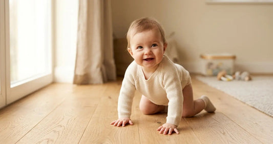 Baby crawling on hardwood floor in hands-and-knees position looking up with a grin