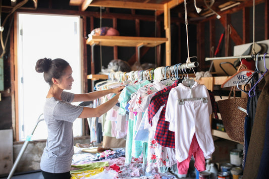 Woman sorts clothing racks at garage sale to sell baby stuff