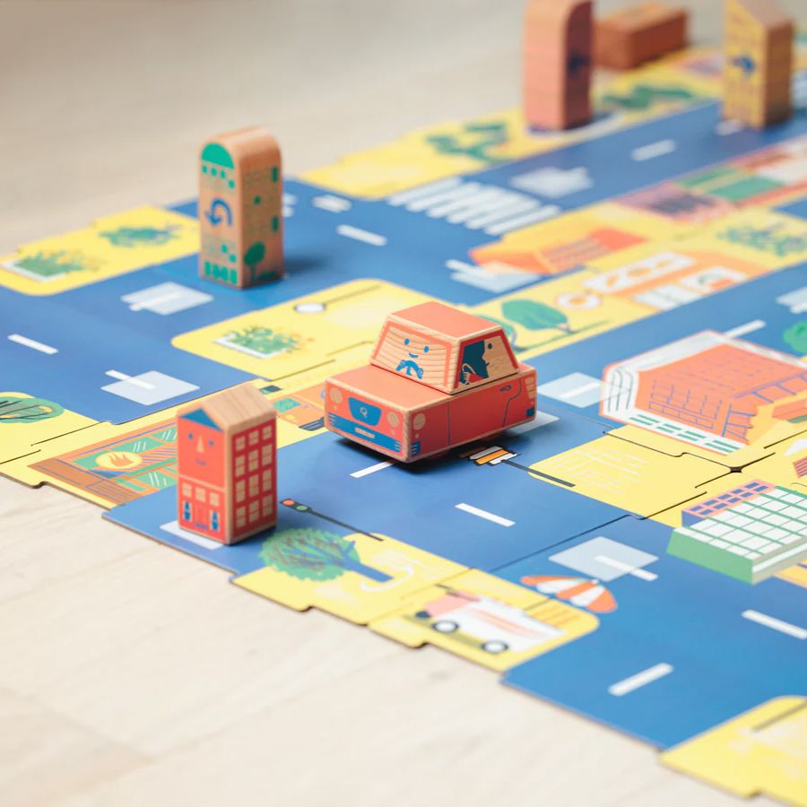 Cody Block City Map street playset with blue roads, yellow buildings, and small wooden block houses and cars on a light wood floor.