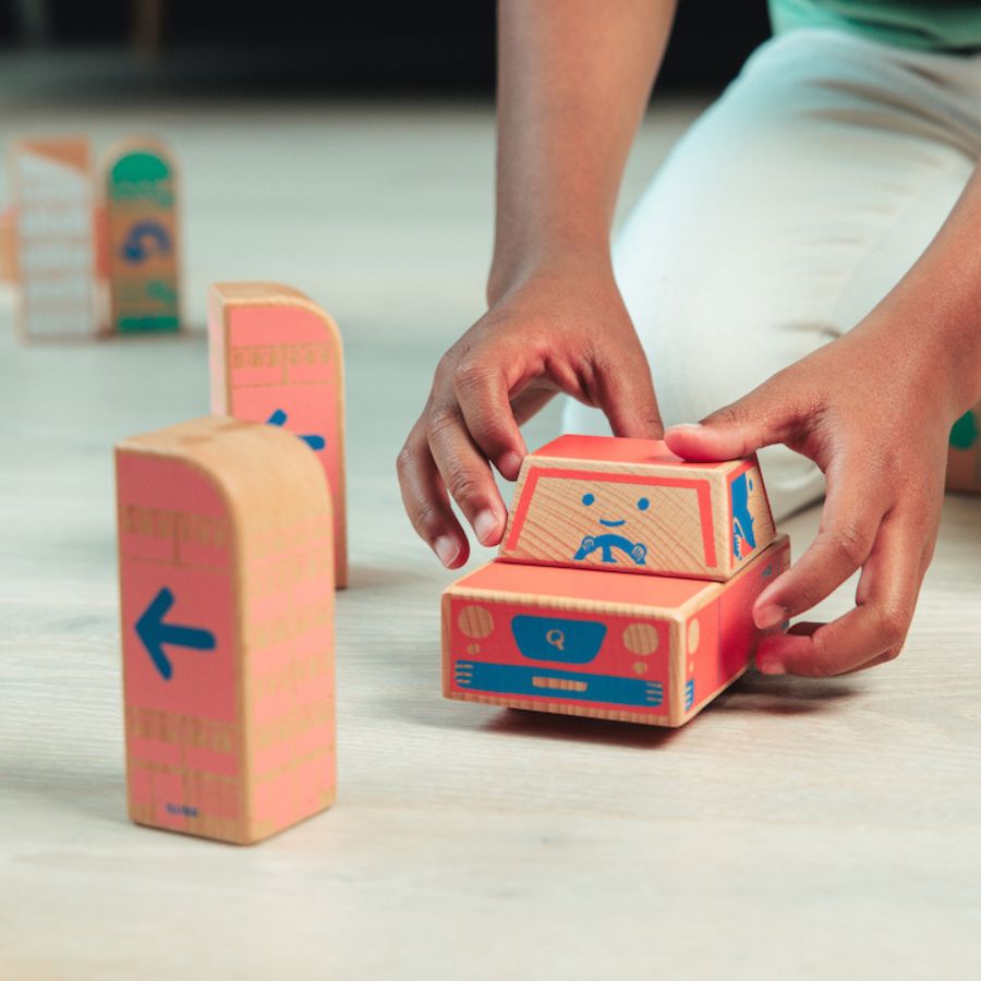 A child's hands are shown holding the Cody Block Car on a light-colored floor, with other blocks standing nearby.