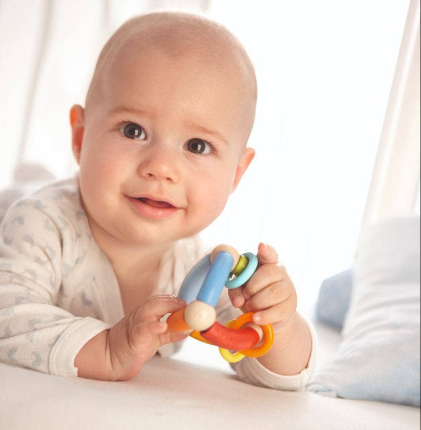 Baby holds HABA wooden clutching toy in triangle shape