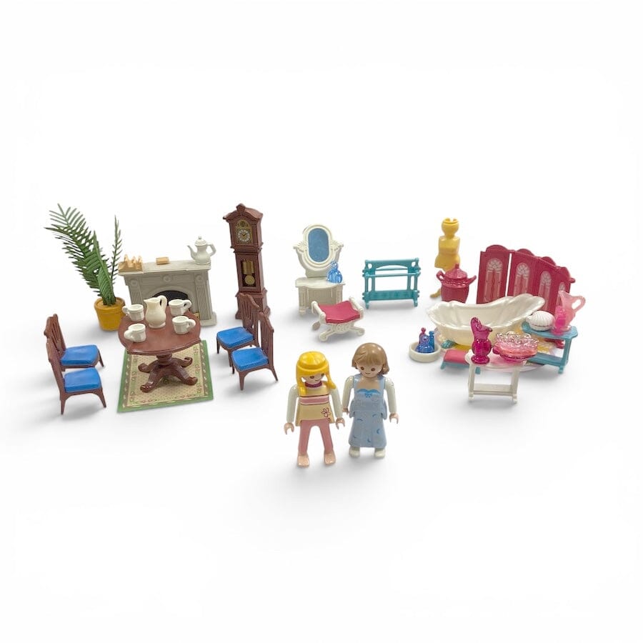 A Playmobil miniature dollhouse-style living room set with two small toy figures, including furniture such as chairs, a table, fireplace, mirror, bathtub, and decor, photographed on a plain white background.