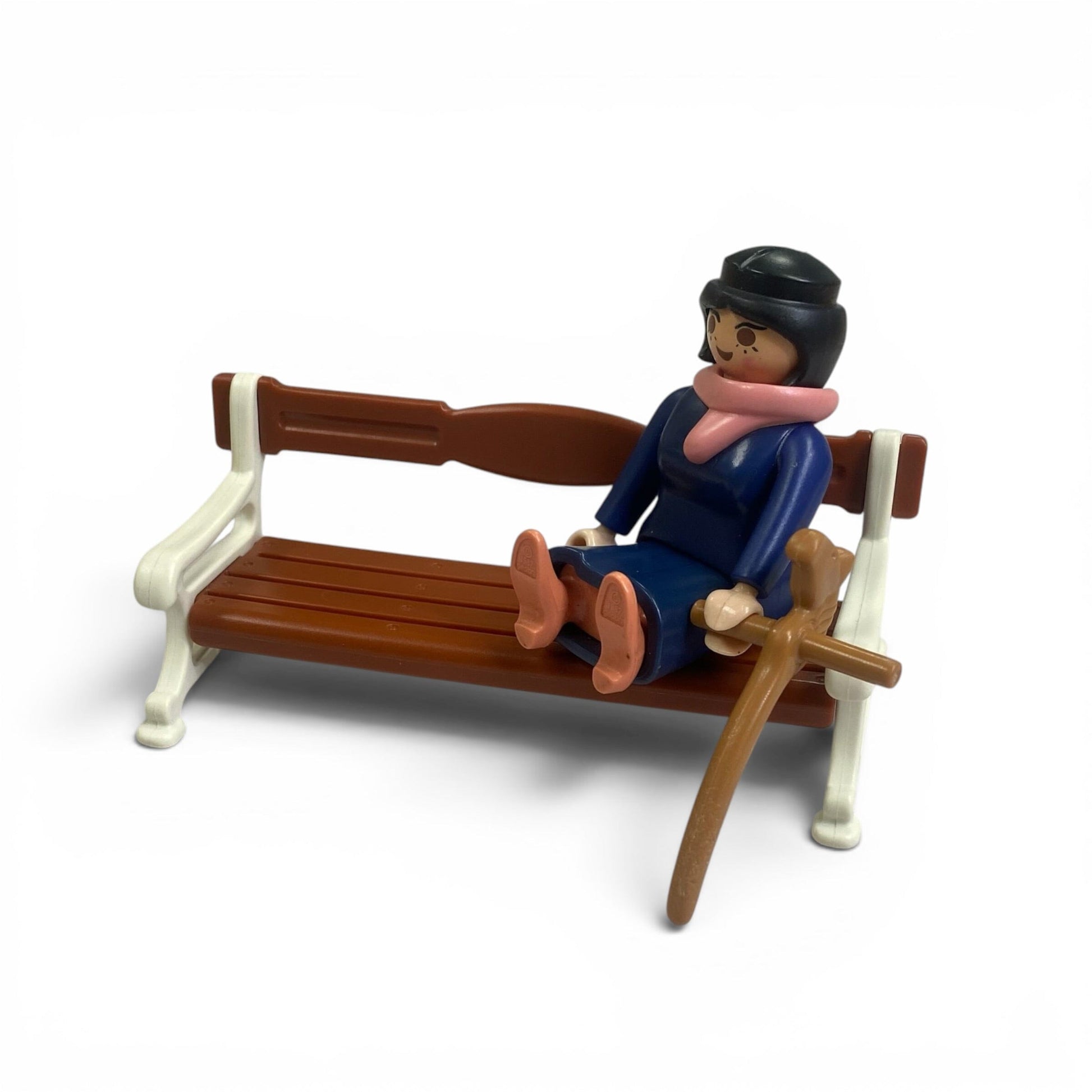 A small plastic toy figure of a seated person on a brown bench with cream-colored armrests, part of the Playmobil Victorian House set photographed on a clean white background.