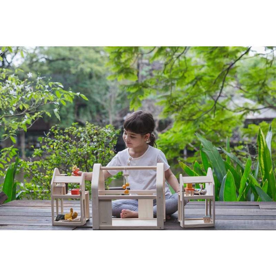 Girl plays with PlanToys Slide N Go wooden Dollhouse and Furniture set - natural unfinished wood and compact design for on-the-go play.