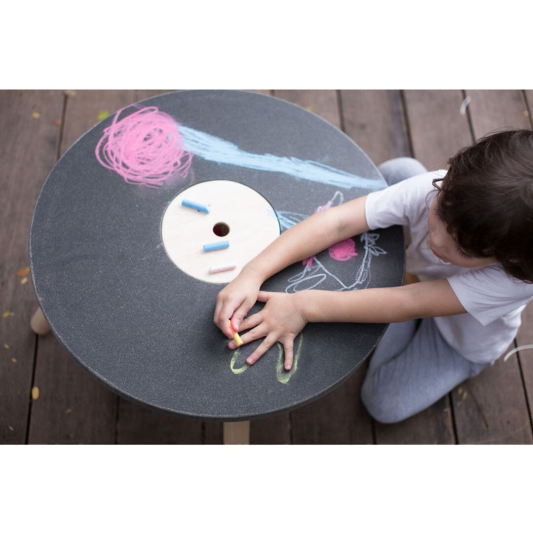 Child draws on PlanToys wooden round table with natural wood unfinished legs and erasable writing surface.